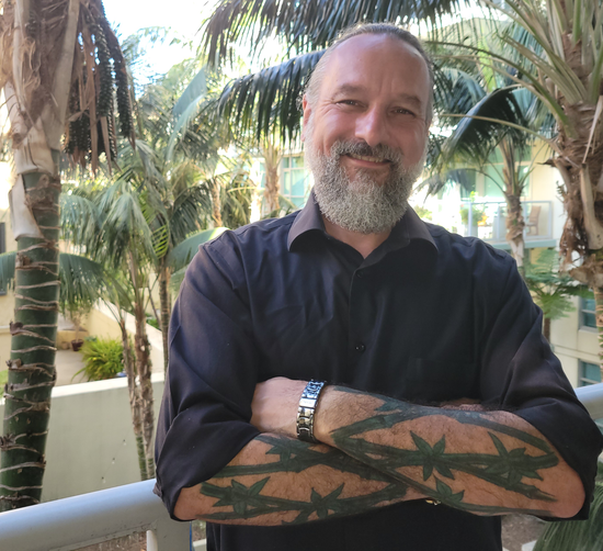 Ralph Hamrick smiling on outdoor balcony in front of palm trees